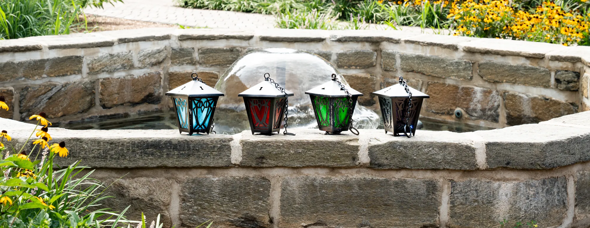 four laterns on a fountain with flowers in the background