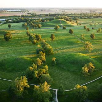 Photograph of Cahokia, showing pathways around two hills with woods in the foreground.