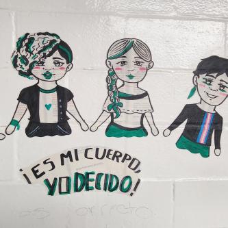 A mural of four figures arched over the words "!Es Mi Cuerpo, Yo Decido!"