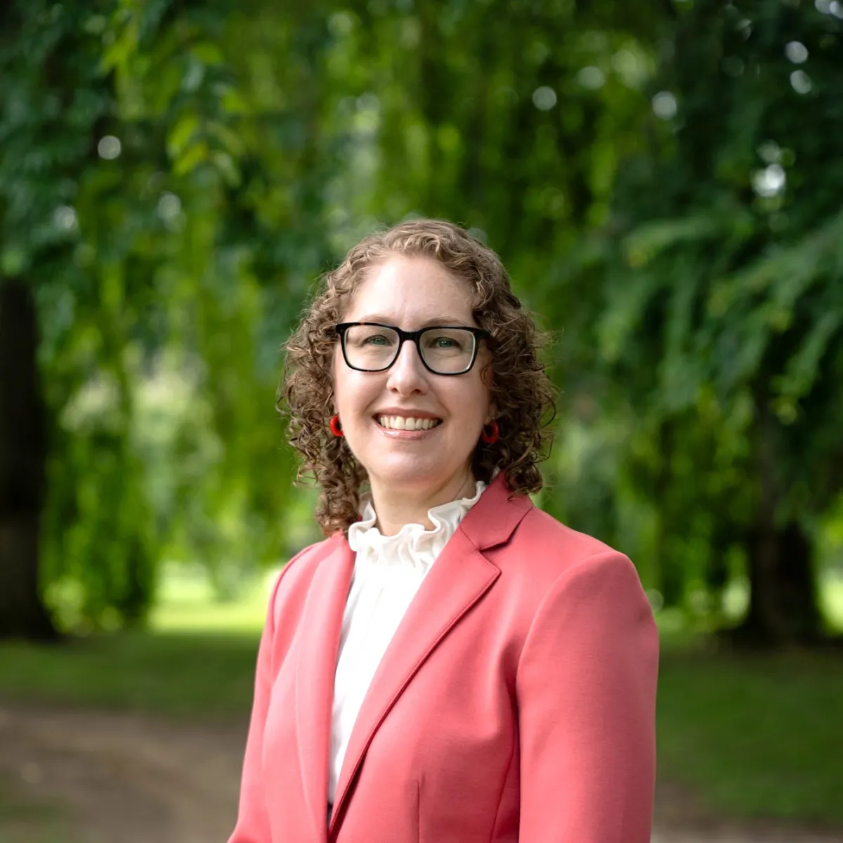 Woman in coral blazer in front of trees
