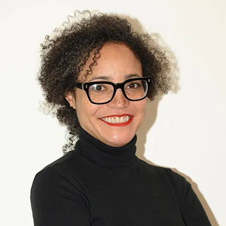 Monique Scott smiles at the camera in a headshot in front of a white wall. Her hair is loosely pulled back, and she is wearing a black turtleneck and black-framed glasses.