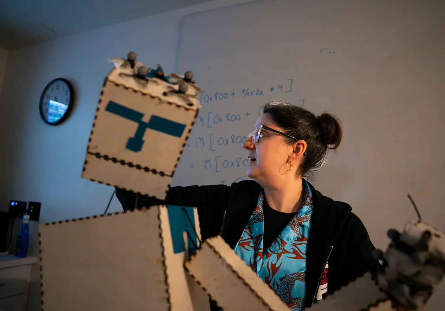 Aline holding a paper robot that is tracking on a screen behind her