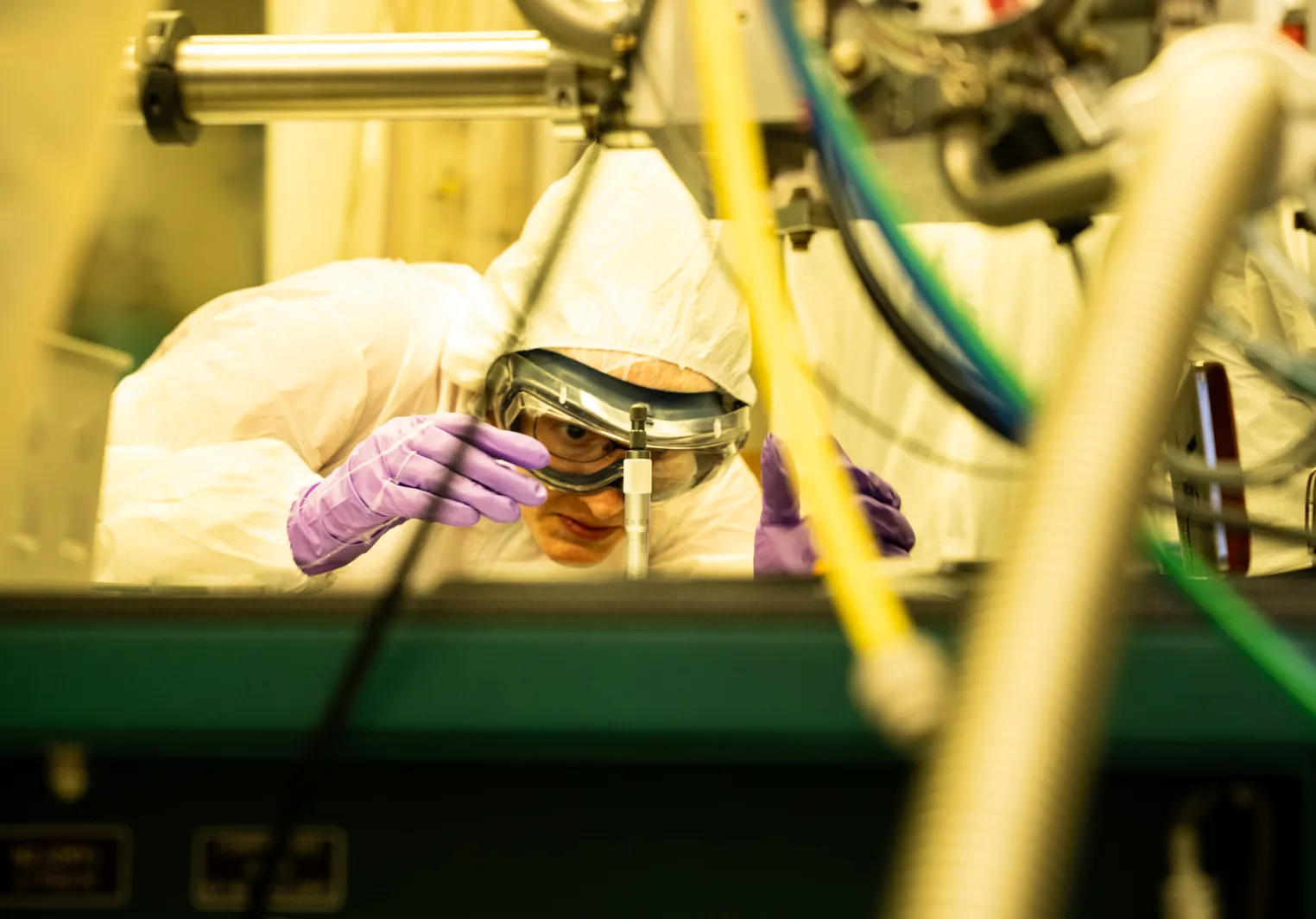 a scientist in full body protective gear squints close to a piece of equipment