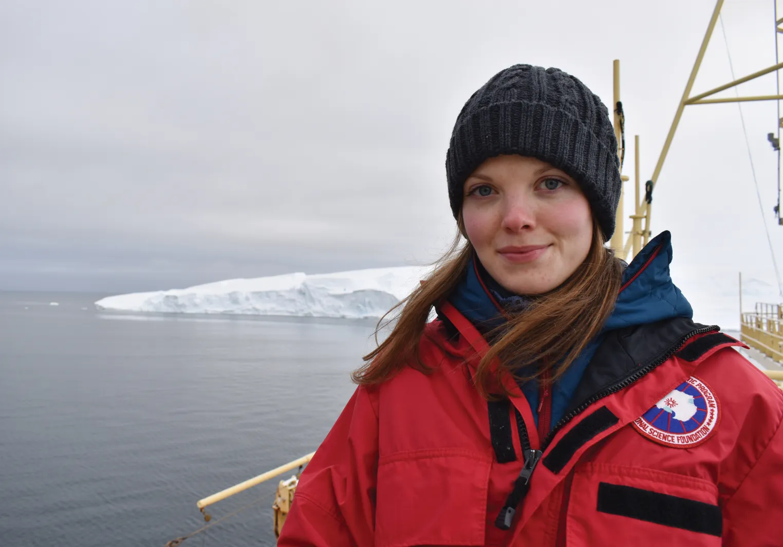 Light skinned woman with long hair wearing a heavy red jacket and a black hat on a research boat in the Southern Ocean