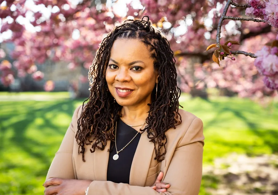 Woman in tan blazer standing in front of tree