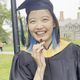 Student in cap and gown smiling and holding a small microphone