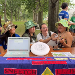 Three students wearing a bucket hat behind a Sneetch Ultimate club table 