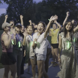 A group of students wearing green light sticks waving and smiling