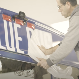 Man installing "Blue Bus" lettering on the back of a bus