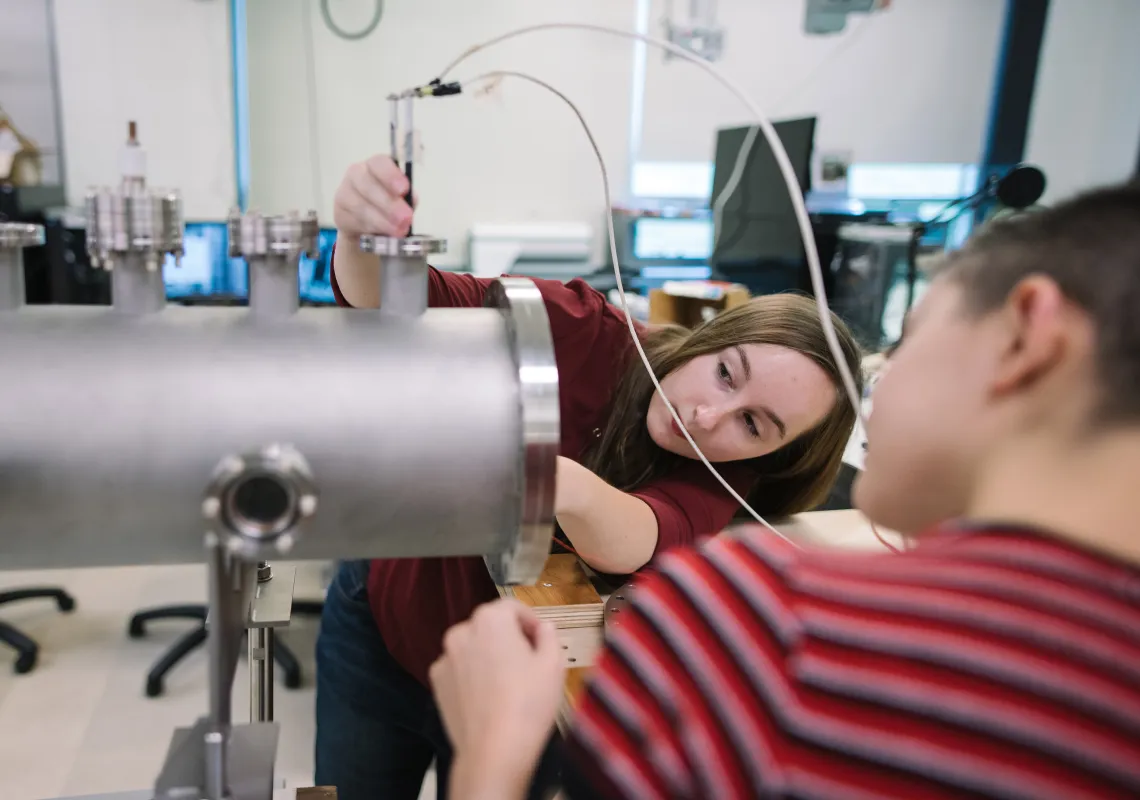 Two physics students work on plasma physics equipment in a lab
