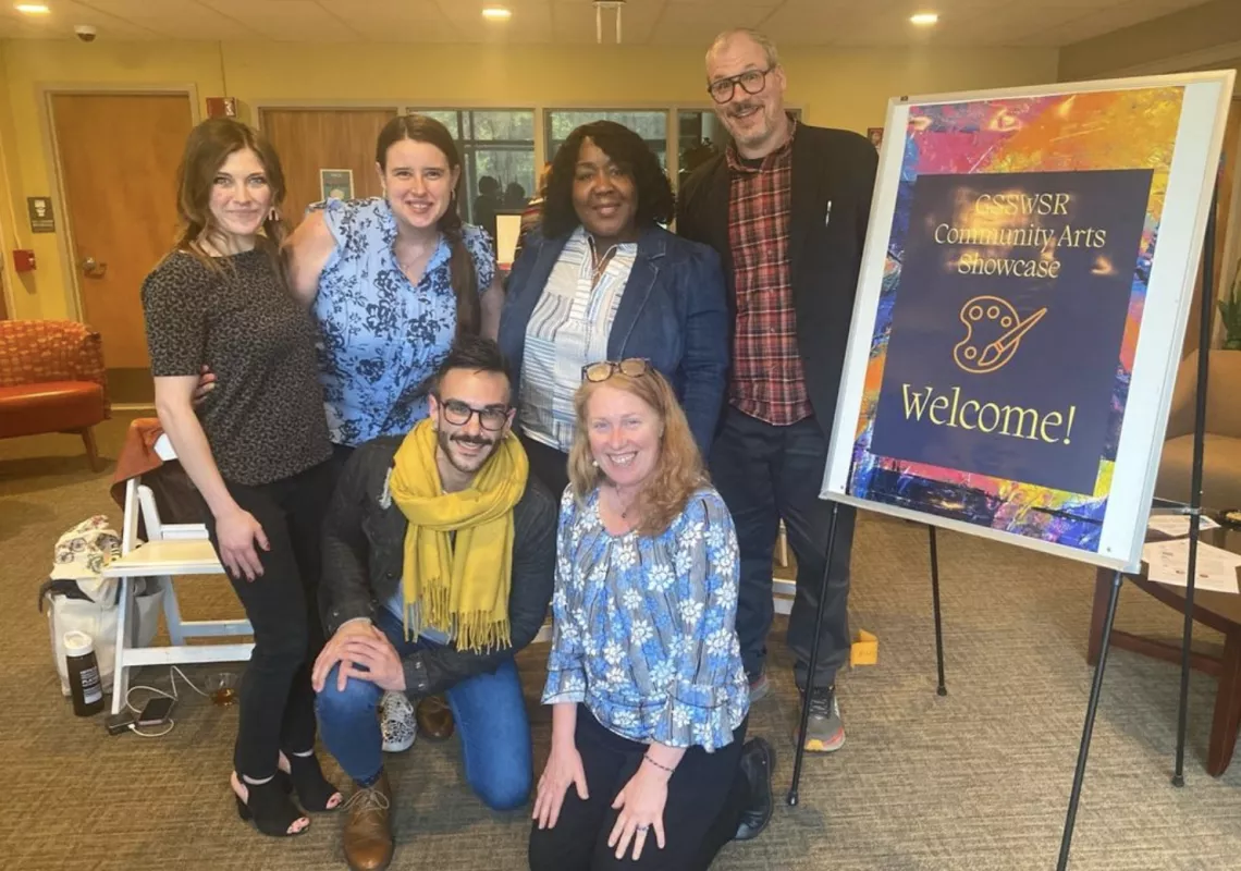 Six members of the Graduate School of Social Work and Social Research posing in a group photo in front of a "GSSWSR Community Arts Showcase Welcome!" sign