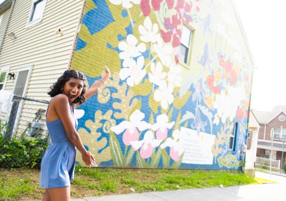Lakshmi Natesan '25 posing in front of a floral mural by Mural Arts Philadelphia