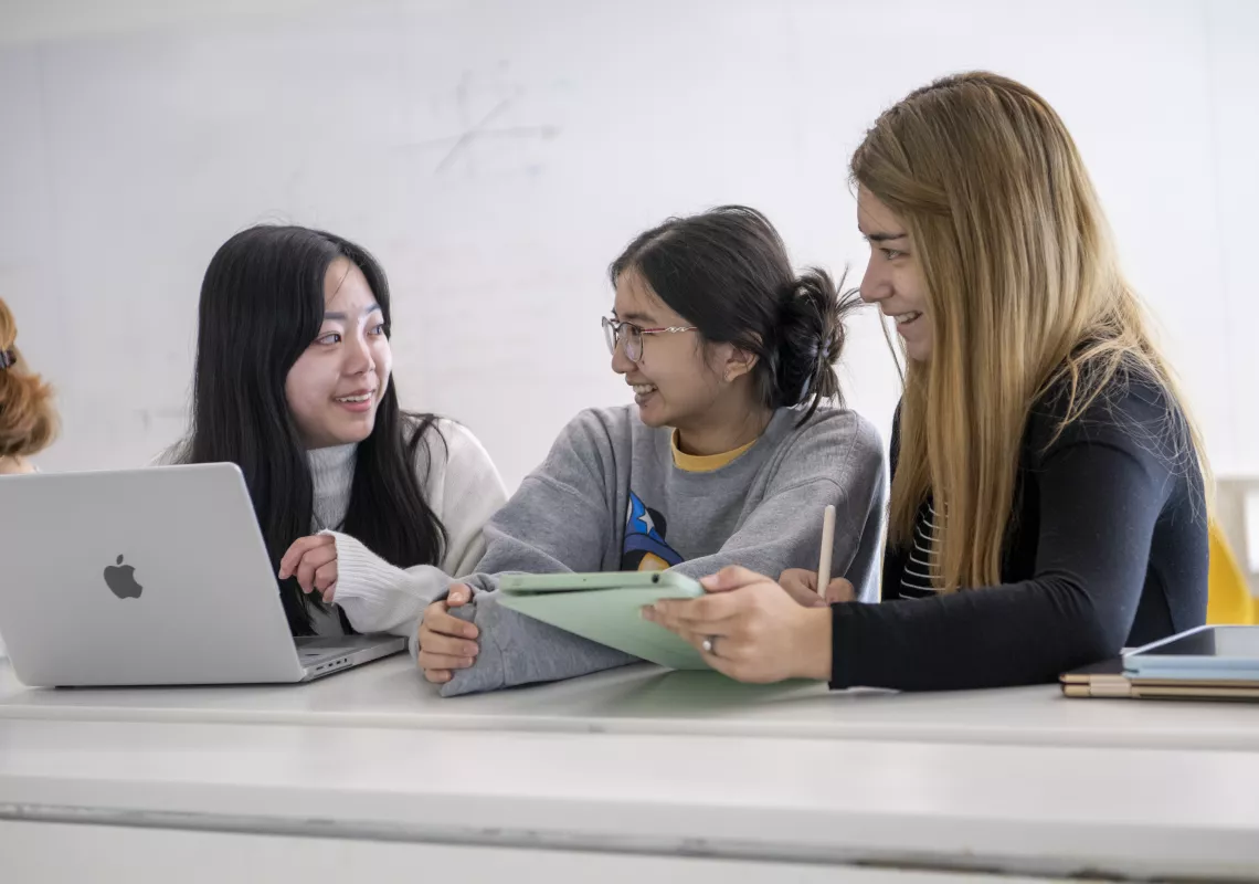 Students smiling at each other while holding a laptop and iPad