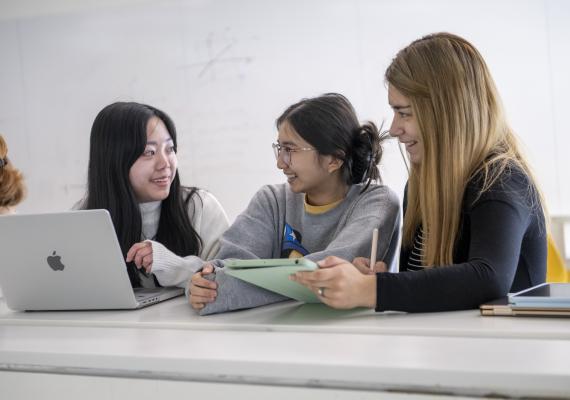 Students smiling at each other while holding a laptop and iPad 