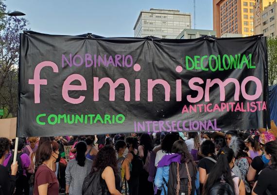 hand-painted banner reading "feminismo" held by women at an outdoor march
