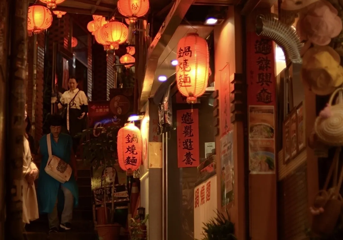 an image of a narrow street in Taiwan at night, lit by many warmly-colored lanterns