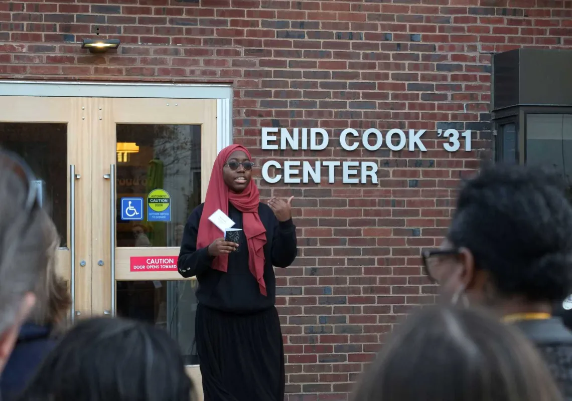 A student stands in front of the Enid Cook Center, talking to a crowd