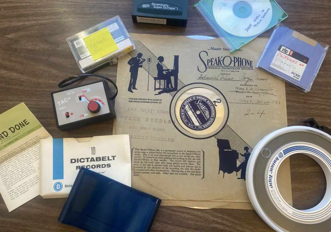 A record, CD, tape, floppy disk, and other assorted old or obsolete media types sitting on a desk. 