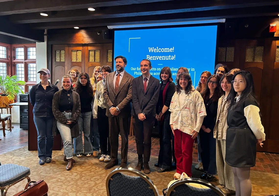 Students stand with instructor and guest speaker in front of a projector screen