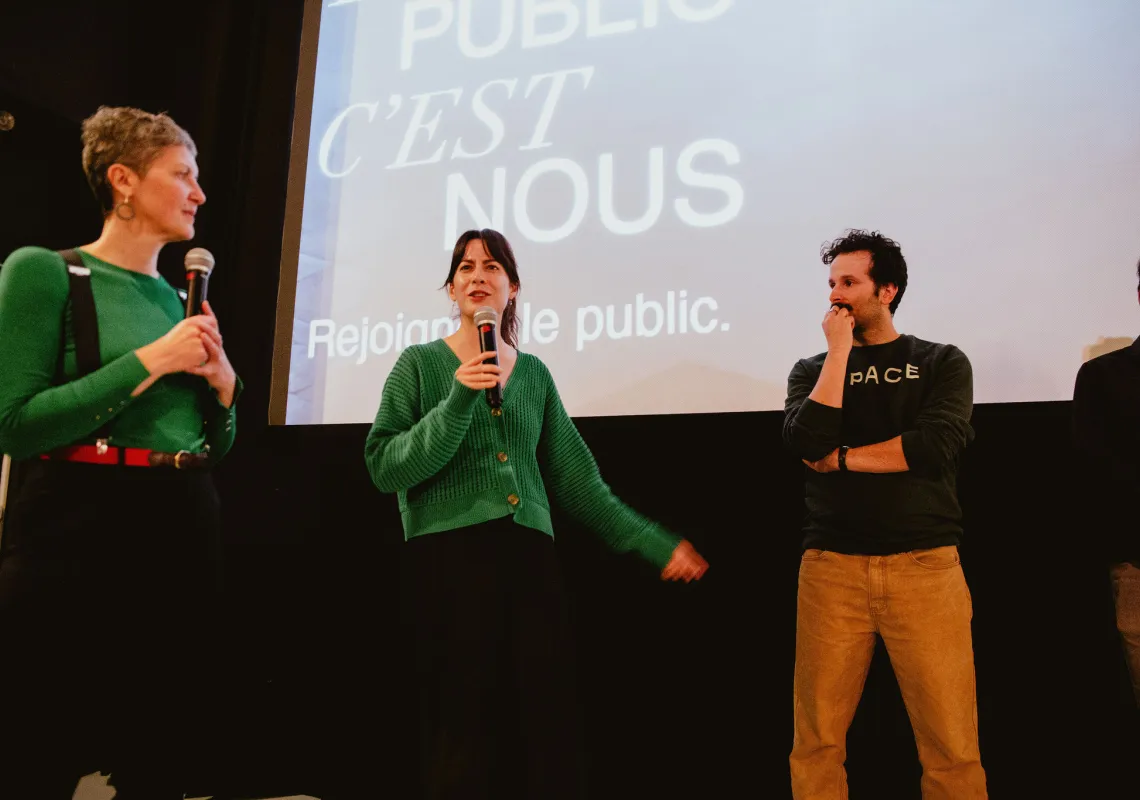 Gen, Aidan, and another participant listen stand on stage and listen to each other.