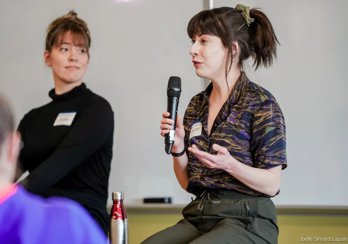 Geneviève Lamoureux holds a microphone and presents at the front of a room