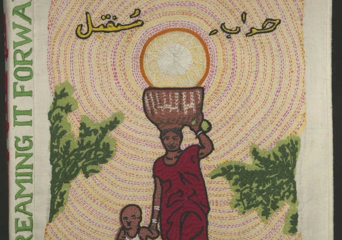 Cloth book with the words "Dreaming It Forward" stitched on the spine. The front image is a woman carrying a basket on her head while holding the hand of a child. There is Urdu text above her. 