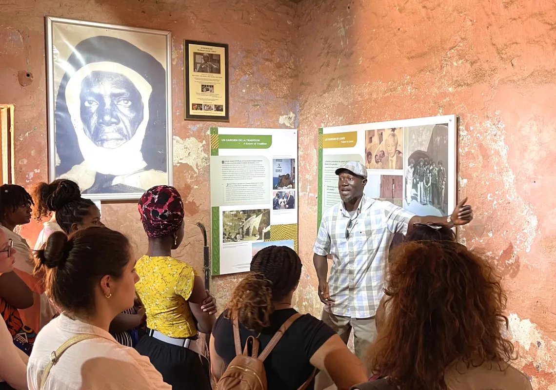 A group of students with their backs to camera listen to a tourguide in a museum.