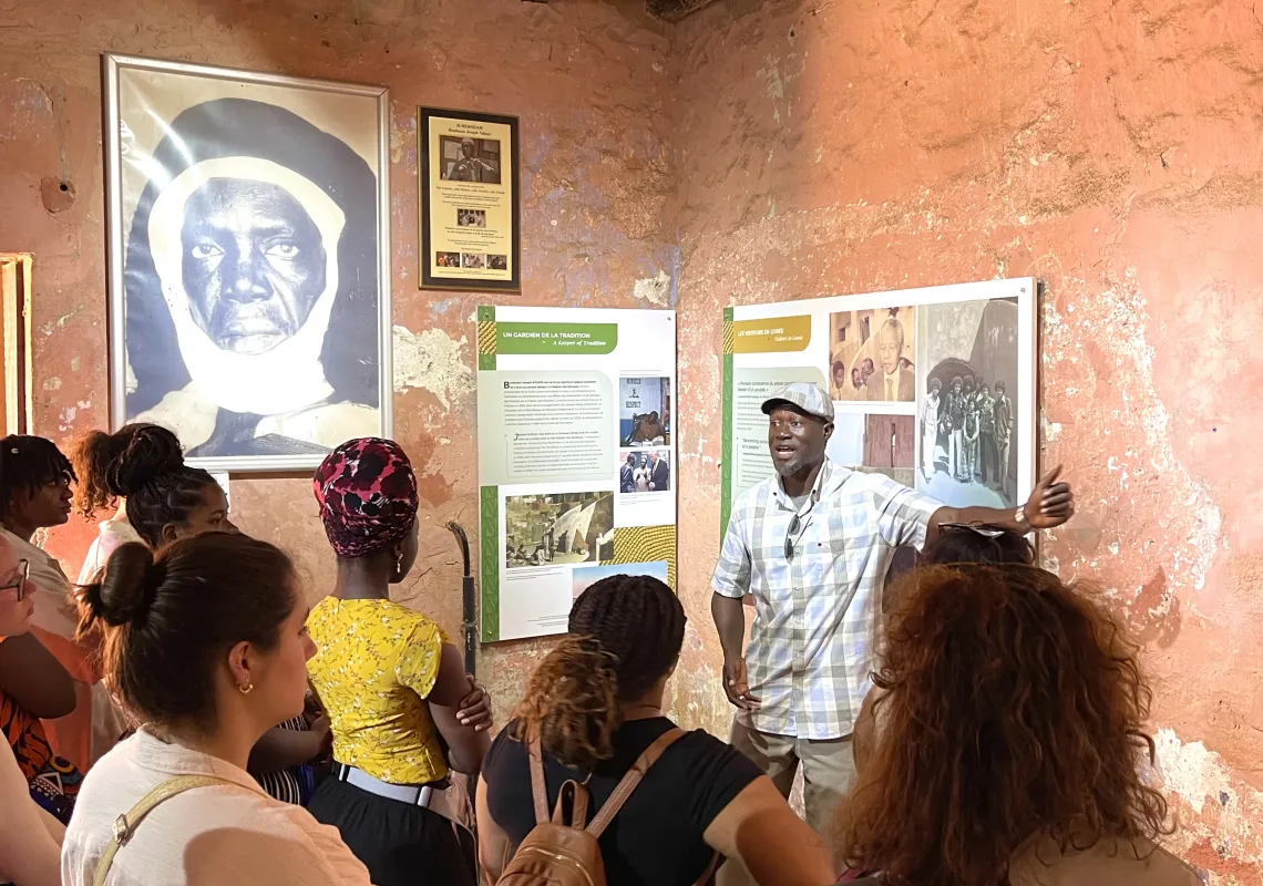 A group of students with their backs to camera listen to a tourguide in a museum.