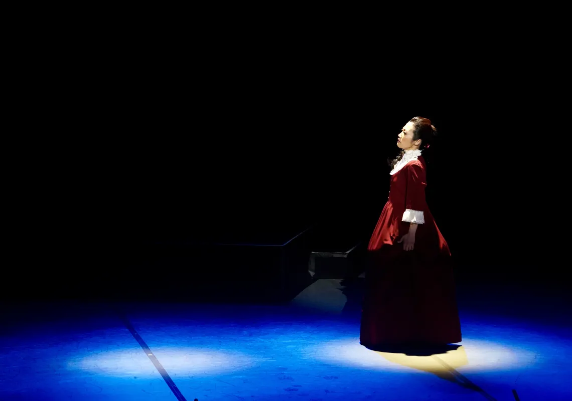 The character of Umeko Tsuda stands on a dark stage