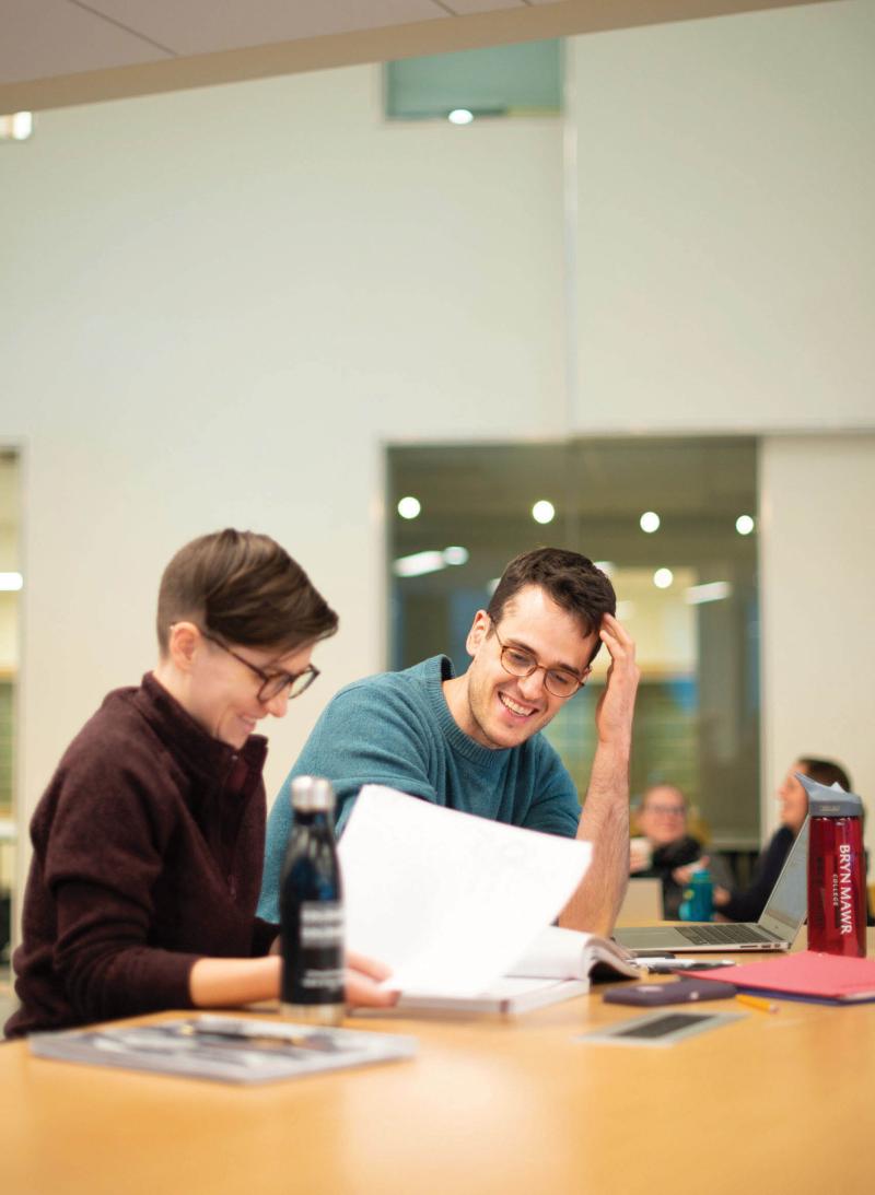 Two students smiling while studying at a table