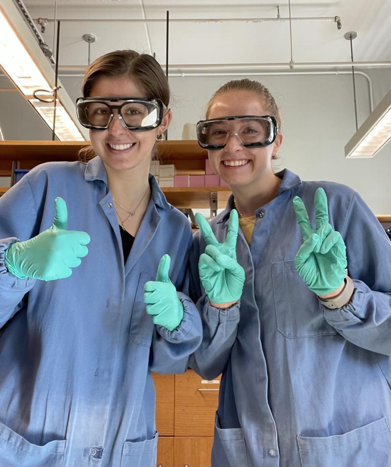 Yael and research partner in the lab wearing lab coat and gloves