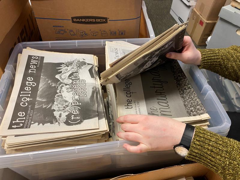 A student researcher looks through a large plastic bin full of back issues of The College News.