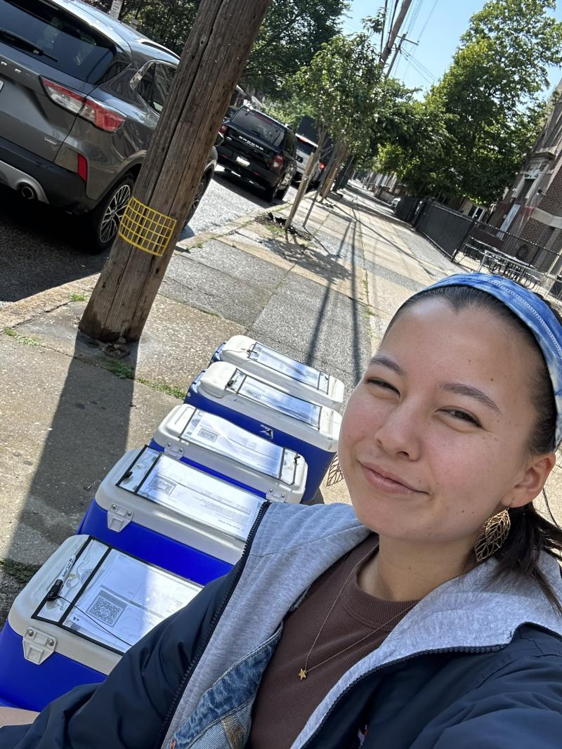Amy taking a selfie amongst coolers on a street. 