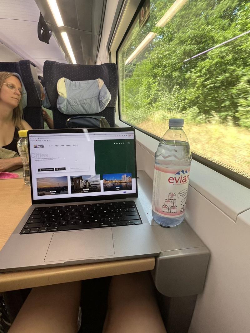 Train with a laptop and a water bottle on tray table. 