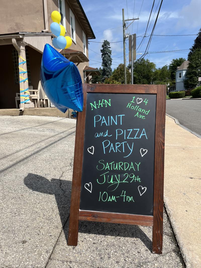 Street A-sign that reads "Paint and Pizza Party Saturday July 29th 10 AM - 4 PM"