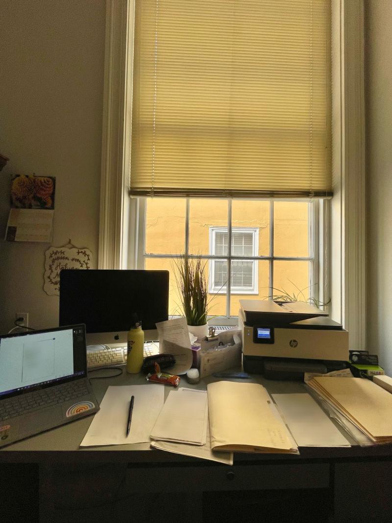 Desk with papers and a laptop in front of a window. 