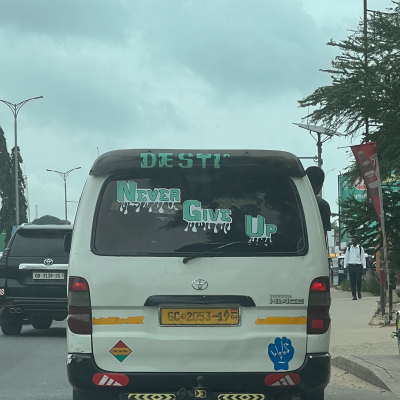 Back of a car with "never give up" written on the window. 