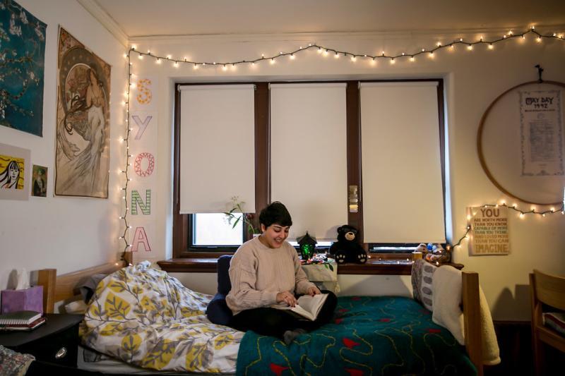 Student sitting on bed in dorm room