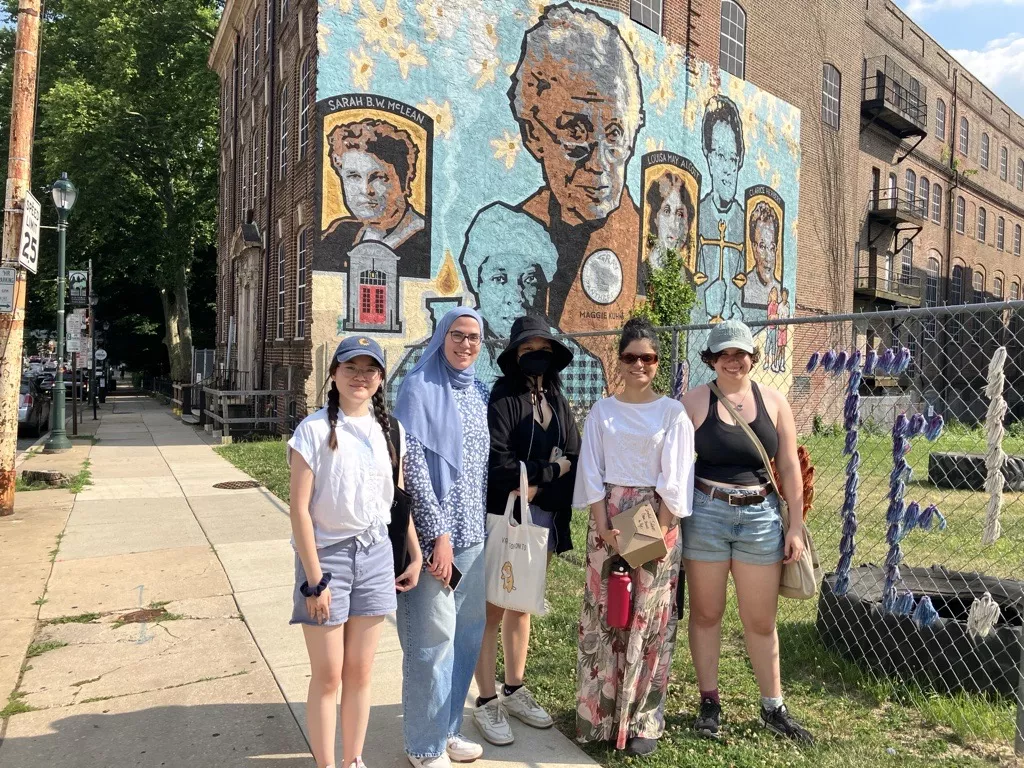 The 2024 Digital Scholarship Summer Fellows standing in front of the mural painted on the side of the Germantown YWCA building.