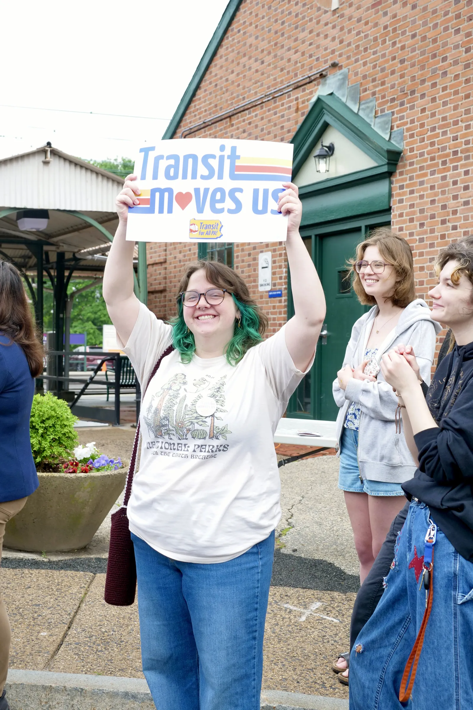 Katie holds a sign that reads "Transit Moves Us"