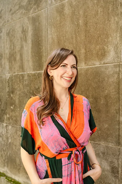 Emily Alesandrini in orange and pink shirt in front of concrete wall