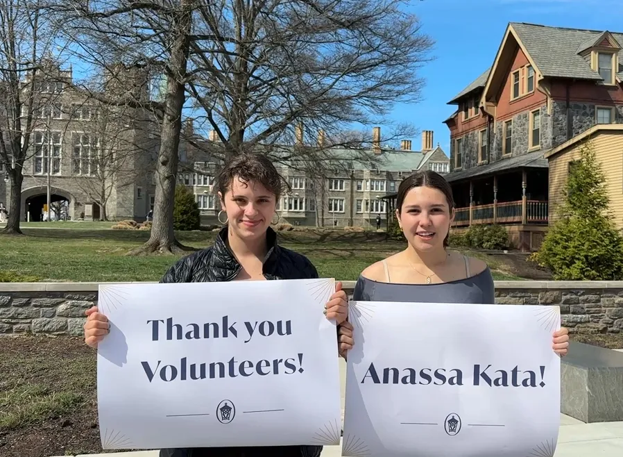 Two Bryn Mawr students holding Thank you volunteers and Anassa kata signs