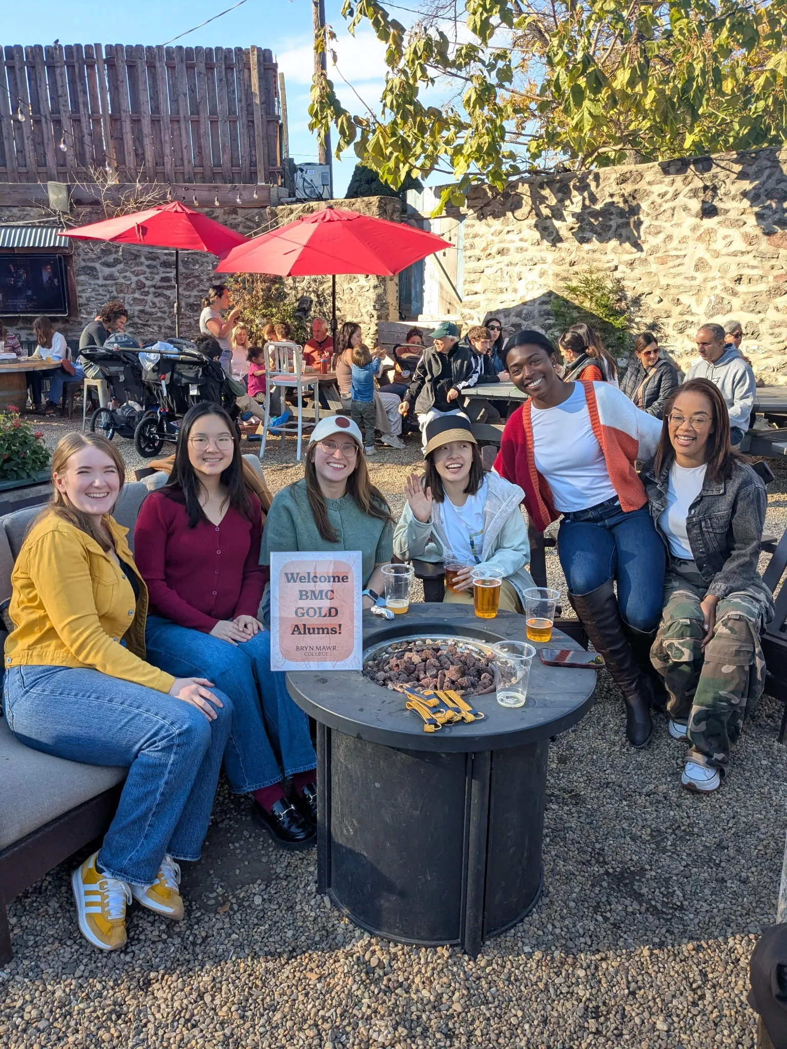 A group of young women sit around a fire pit and smile at the camera